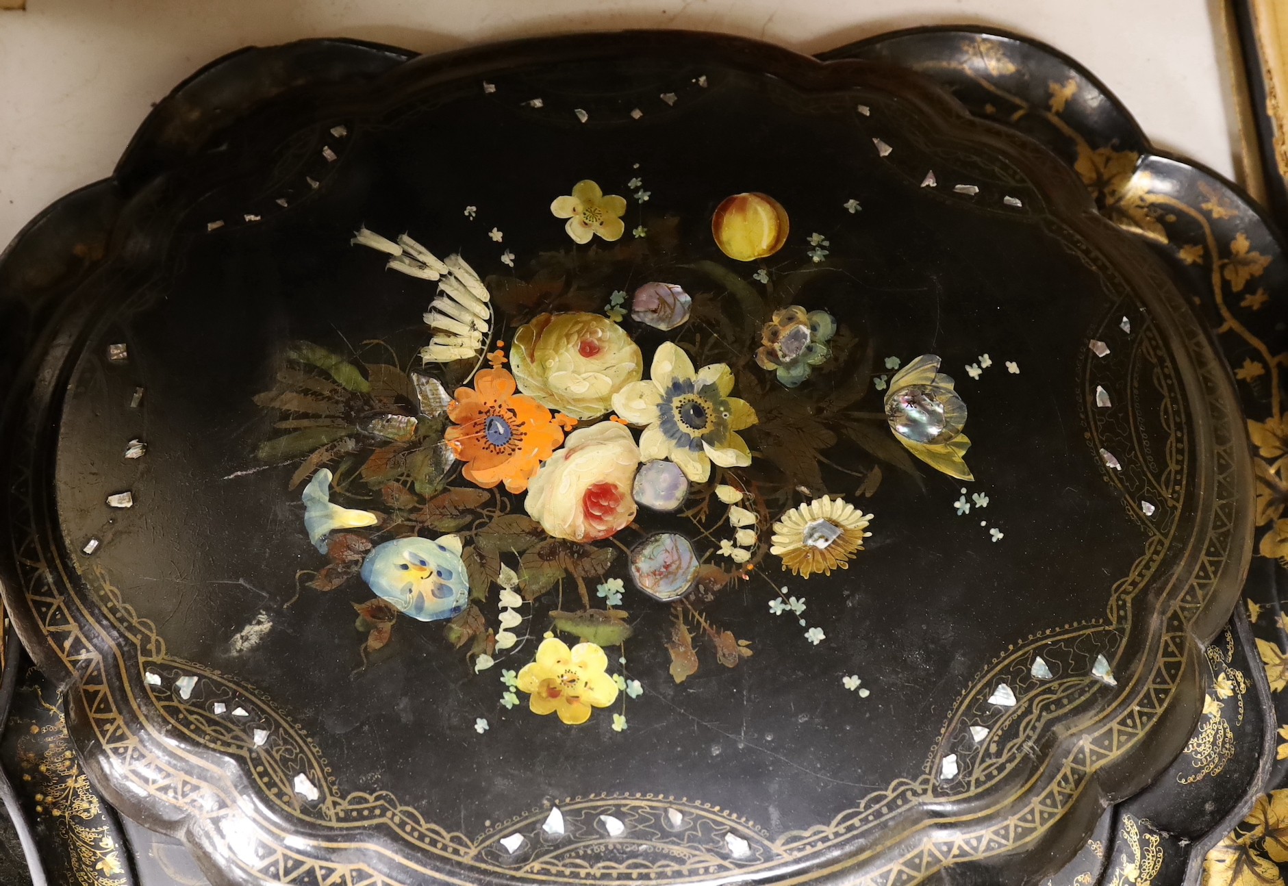 Four papier-mâché-mâché trays, a roundel and bowl, largest tray 80cms wide